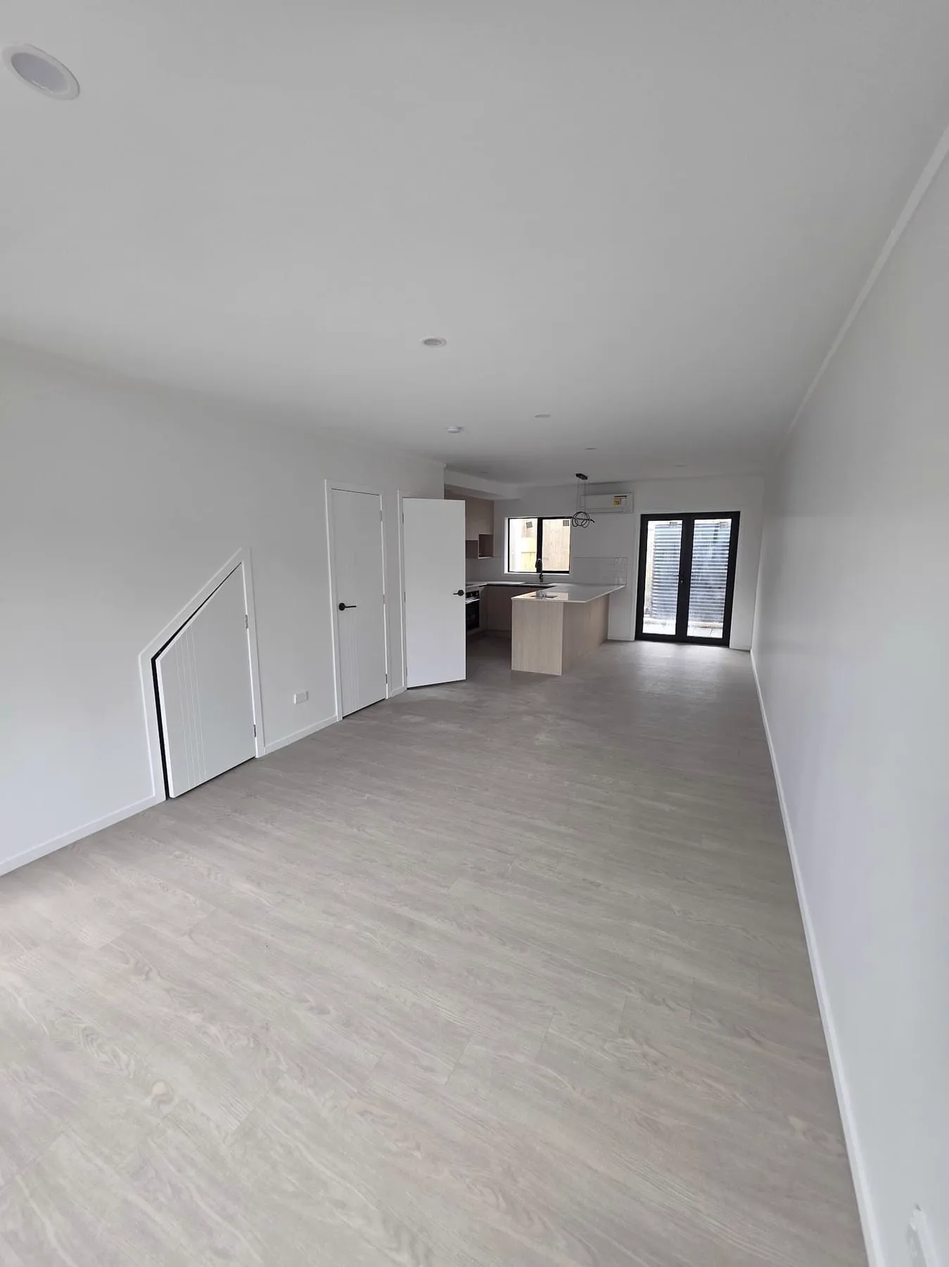 The same open plan living area from the other end, showing the plank flooring continuing flush past two doorways and into the kitchen