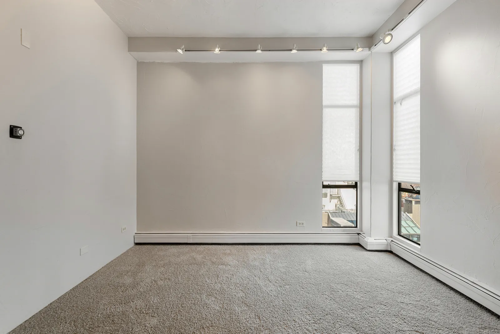 Empty bedroom with grey carpet laid wall to wall and a window with a roller blind