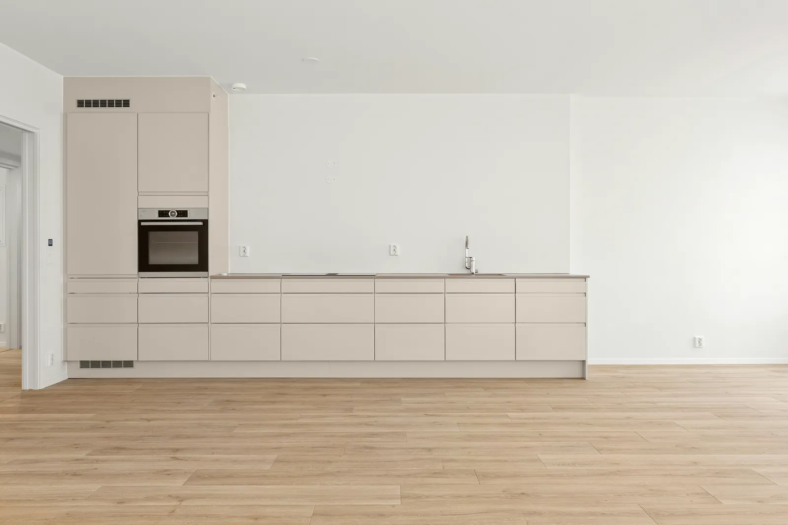 Empty modern kitchen with light wood look plank flooring running from the cabinetry into the living space