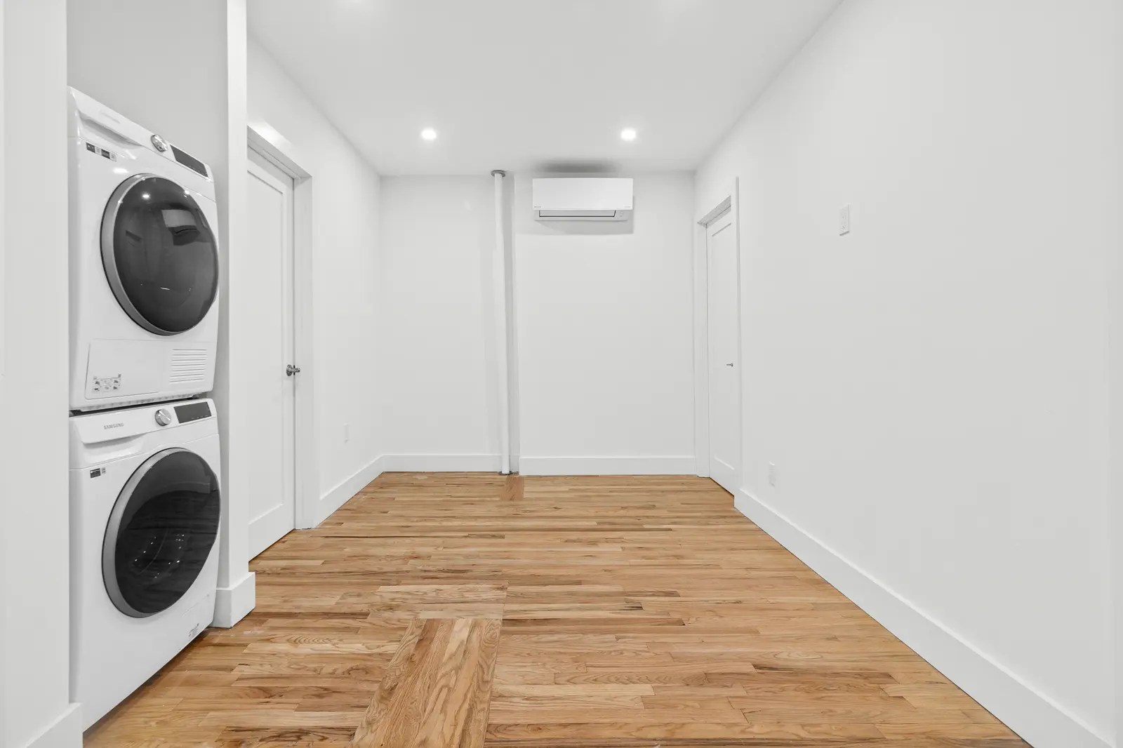 Laundry room with a stacked washer and dryer on light oak wood-look plank flooring
