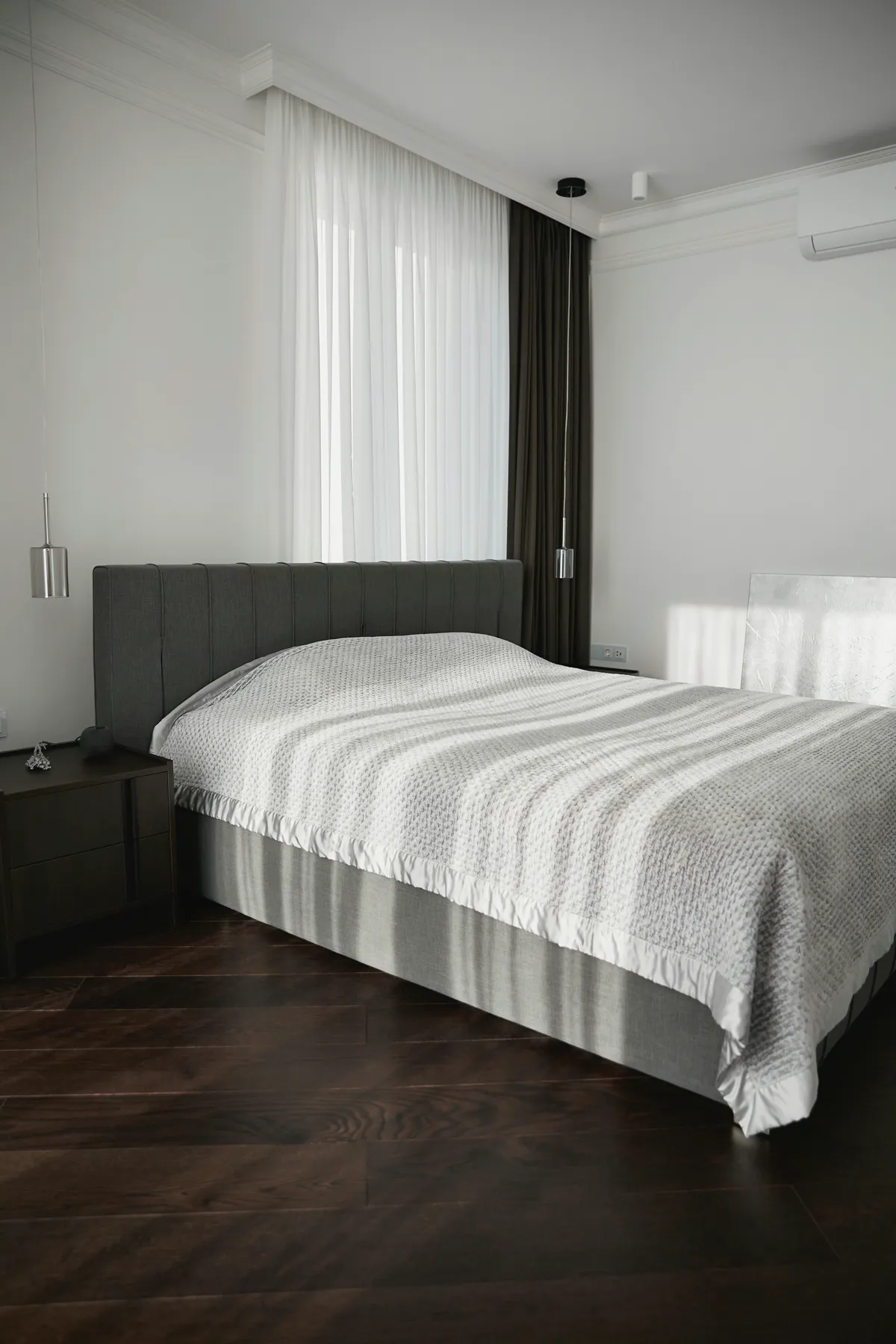 Modern bedroom with dark walnut plank flooring, an upholstered bed base and sheer curtains