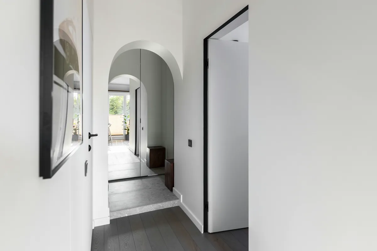 Minimalist arched hallway with dark timber flooring and a round mirror