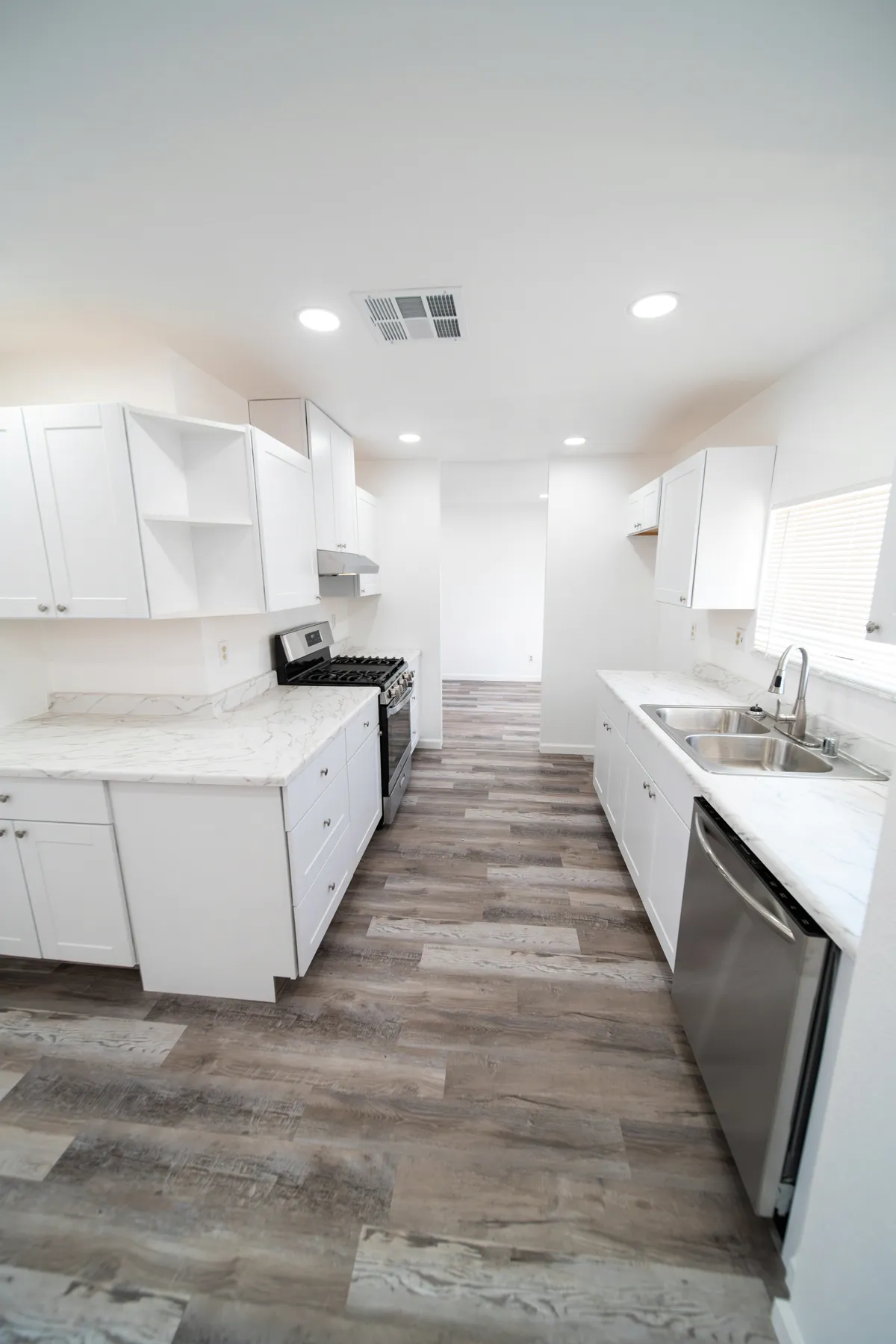 Galley kitchen with white cabinetry and grey wood look plank flooring running the length of the room