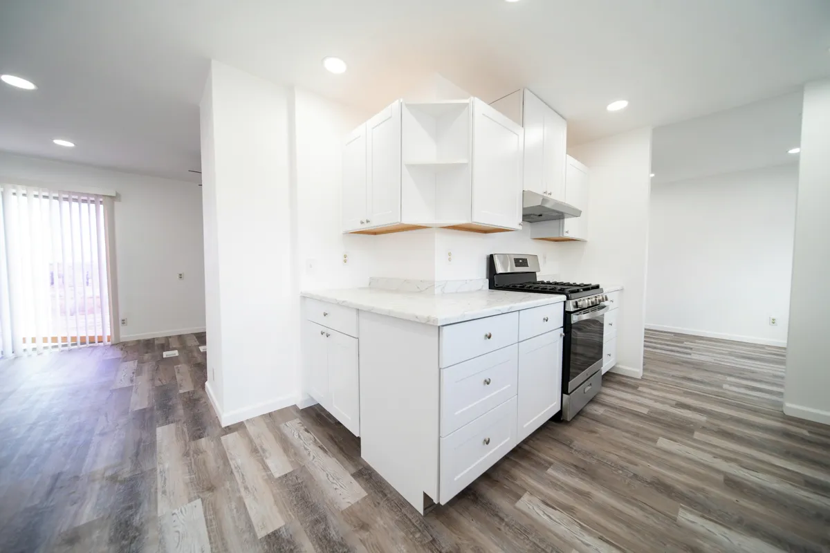 Open plan kitchen with white cabinetry and grey wood look plank flooring opening onto living spaces on both sides