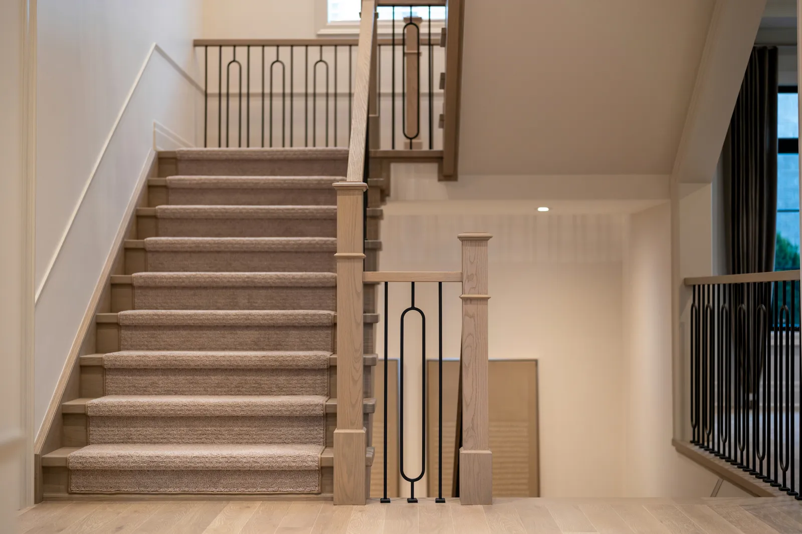 Modern staircase with carpeted treads and dark metal balusters against oak newel posts